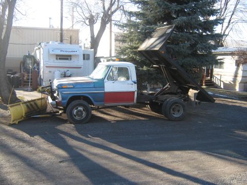 1972 Ford F-250 - A side view of a dump truck equipped with a snow plow, its bed in a raised position.