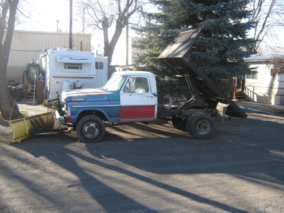 Dump truck with a snow plow, painted blue, white, and red, with its bed raised