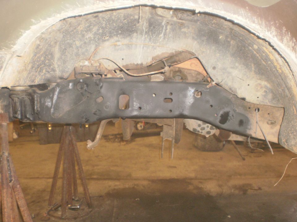 Vehicle frame and suspension parts on jack stands, showing rust and wear