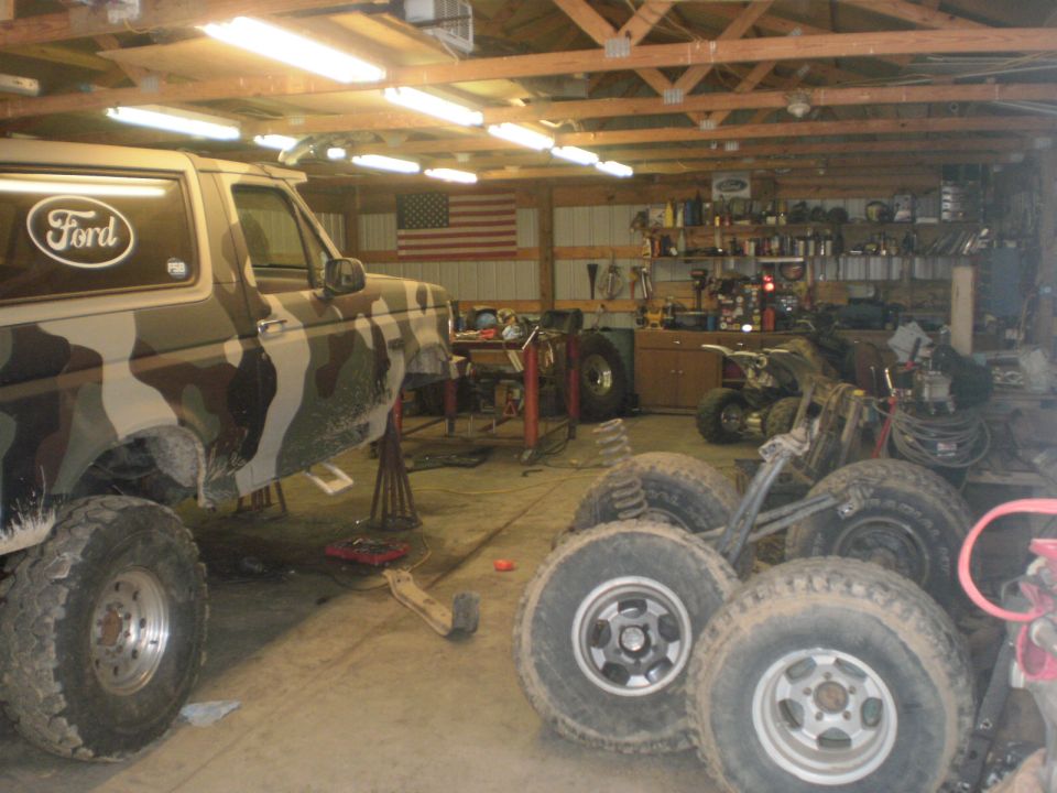 1995 Ford Bronco with camouflage paint on jack stands in a garage, spare tires nearby