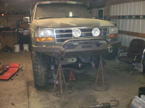 1995 Ford Bronco - A camouflaged Ford Bronco is elevated on jack stands in a garage, showing its front end and custom modifications.