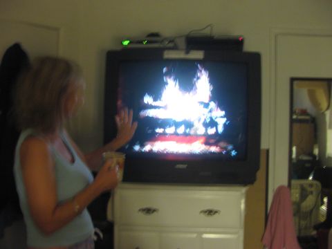 1968 Ford Mustang - Woman watches a television displaying a fireplace scene while holding a cup.