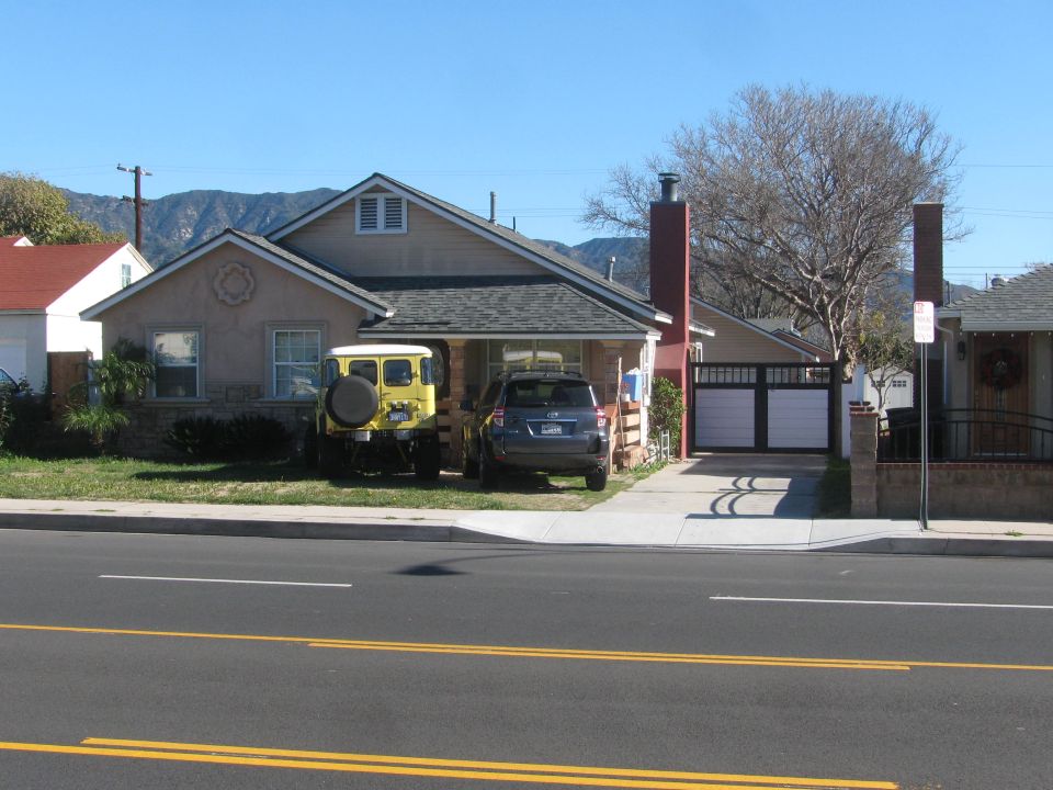 Yellow off-road vehicle with a spare tire on the back, parked next to a dark SUV in front of a house