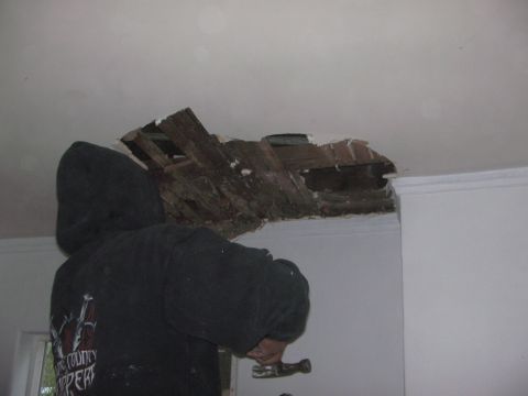 1968 Ford Mustang - A person is actively working on repairing a large hole in the ceiling, exposing wooden beams.