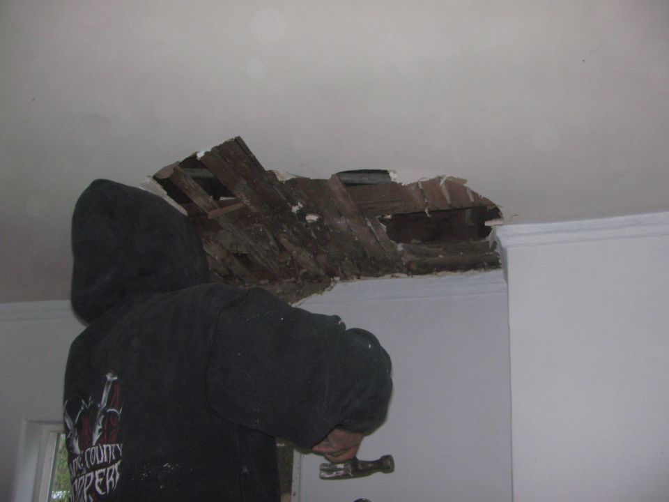 Person in a black hoodie using a hammer to repair a hole in the ceiling