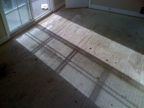 1968 Ford Mustang - Sunlight creates a dramatic shadow pattern across the worn wooden floorboards of an interior room.