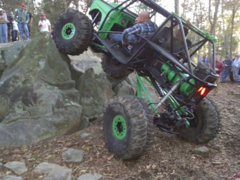 1992 Ford Mustang - A heavily modified off-road buggy navigates a challenging rocky terrain with spectators watching.