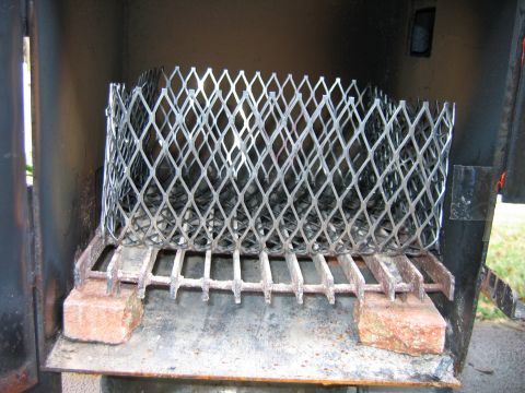 1992 Ford Bronco - The interior of a steel barbecue smoker firebox, holding an expanded-metal charcoal basket that sits on a heavy grate propped up by two fir…