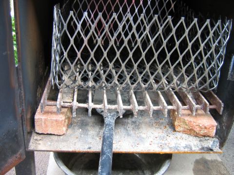 1992 Ford Bronco - Interior of a steel firebox or smoker, showing a curved expanded-metal basket sitting on a slotted grate raised on two bricks, with a shove…