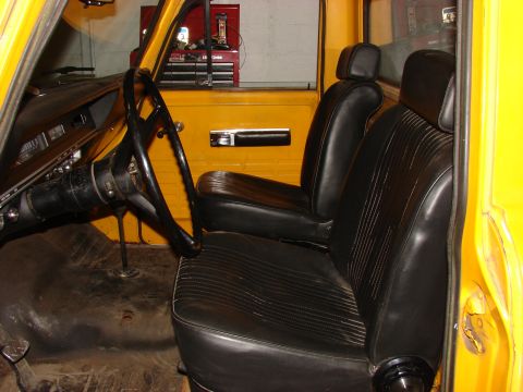 1971 International School Bus - The interior of a yellow truck shows black vinyl seats and a steering wheel, with a red toolbox visible.