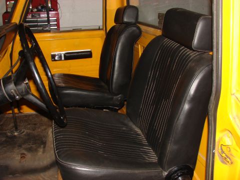 1971 International School Bus - Interior view of a yellow truck cab, black vinyl seats and a steering wheel.