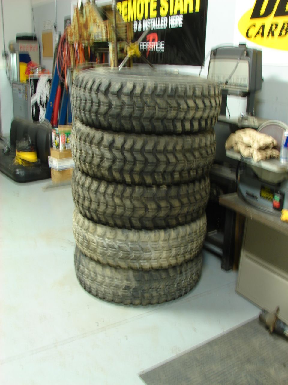 Stack of five used all-terrain tires on a shop floor beside a tire machine
