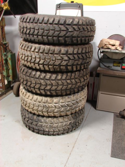1971 International School Bus - A stack of five used off-road tires sits on a concrete floor in a garage.