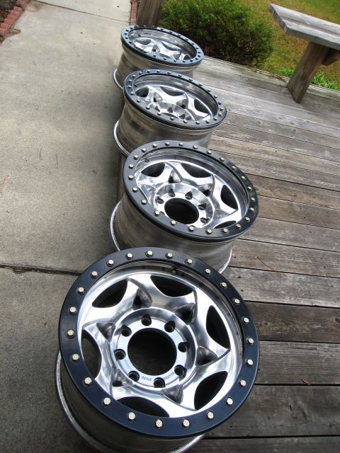 1986 Ford Bronco - Four aftermarket wheels with black beadlock rings are displayed on a wooden deck.