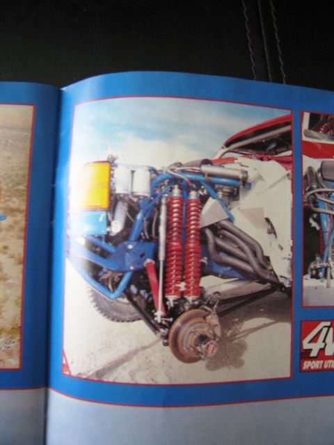 1986 Ford Bronco - Close-up view of the complex front suspension system of a custom off-road vehicle, prominent red coilover shocks.