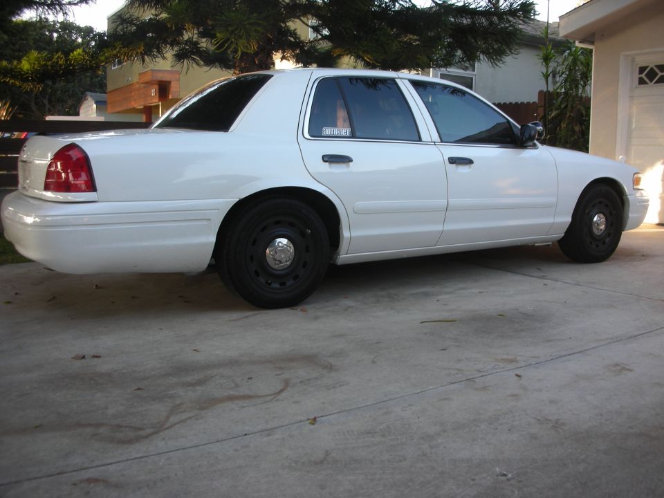 White Ford Crown Victoria sedan, rear 3/4 side view, parked in driveway with black steel wheels.