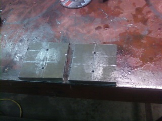1995 Ford Bronco - Metal blocks with markings and holes sit on a workbench, possibly for a vehicle part.