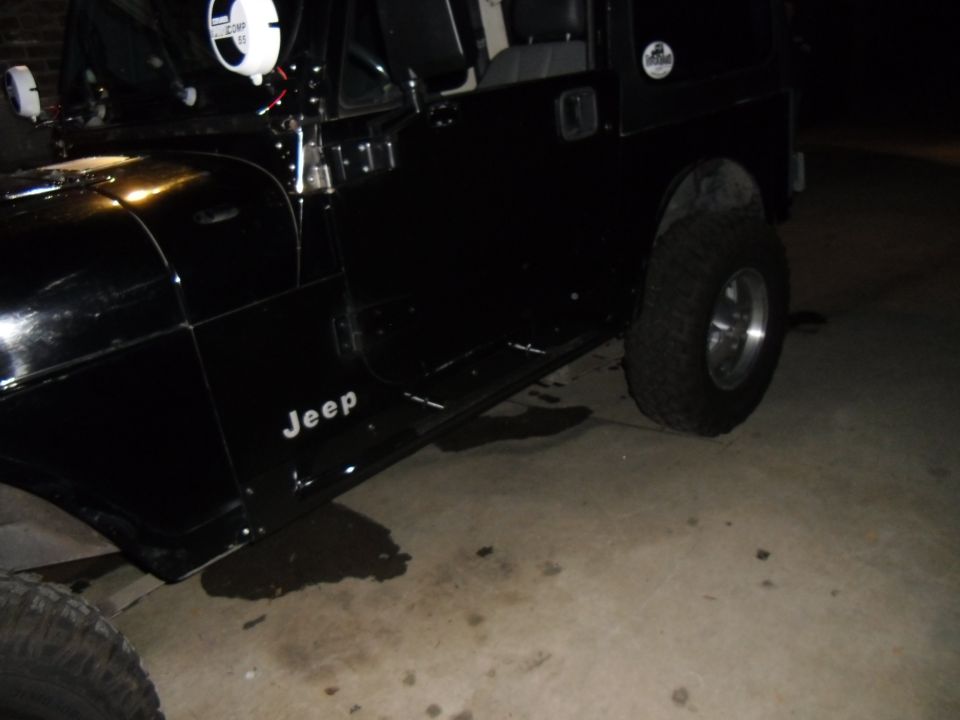 Black Jeep Wrangler side view, showing the door and tire. 'Jeep' text visible on the lower door