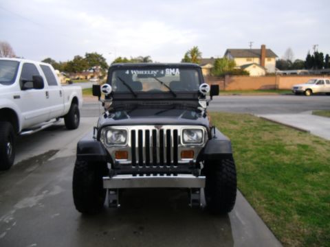 1992 Jeep Wrangler - A black Jeep Wrangler is parked in a driveway, with a white pickup truck to its left.