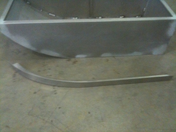 Unfinished metal box-like structure with a curved metal trim piece in front of it
