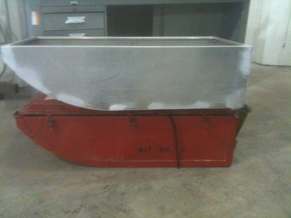 Metal tank sitting on a red container with some text visible on the side