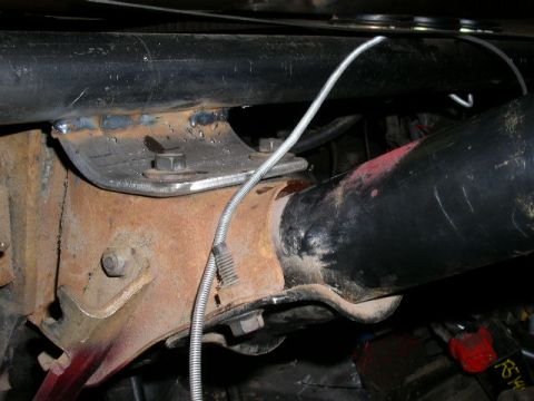 1979 Ford Bronco - The underside of a vehicle shows rusty metal brackets and a large black pipe, likely part of the exhaust or suspension system.