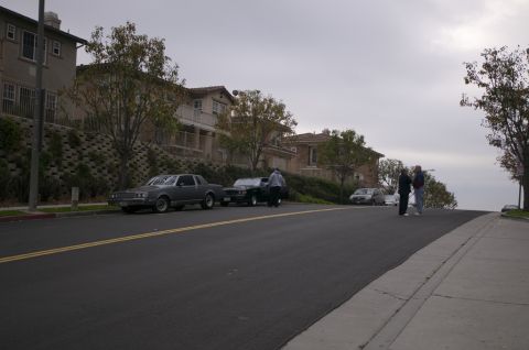 2006 Cadillac STS - Several cars are parked on a street in front of houses on a cloudy day.