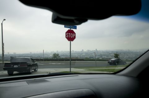 2006 Cadillac STS - Two cars are visible on a road overlooking a city, with a stop sign and street sign in the foreground.