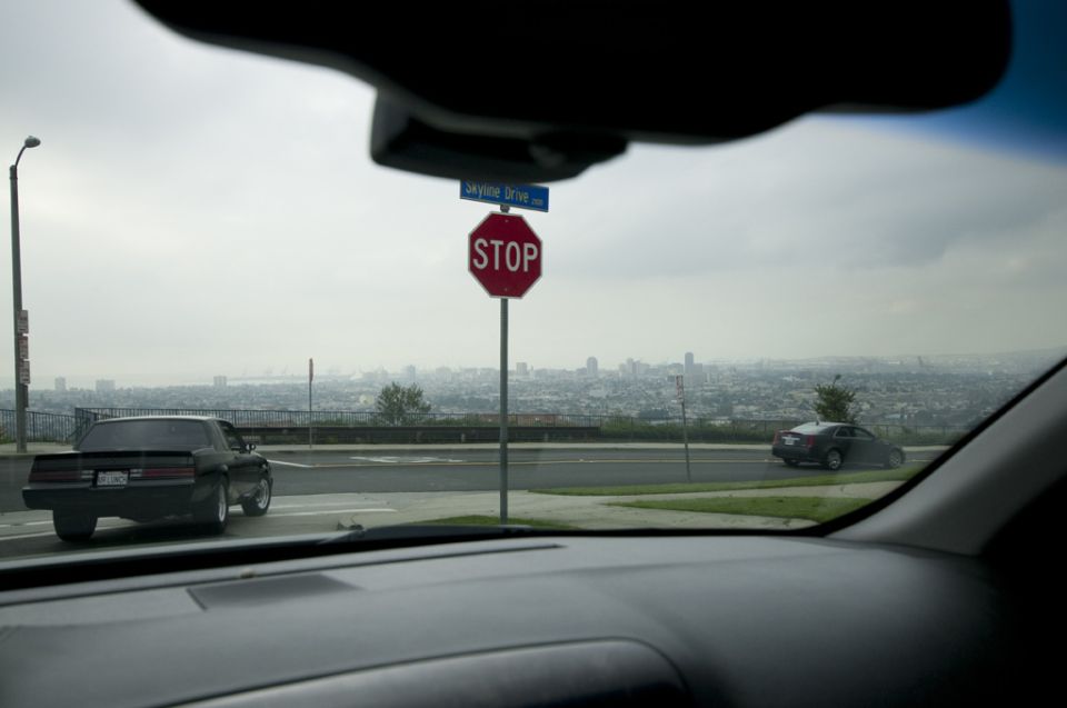 View from inside a car looking out at two other cars on a road, with a city skyline in the distance