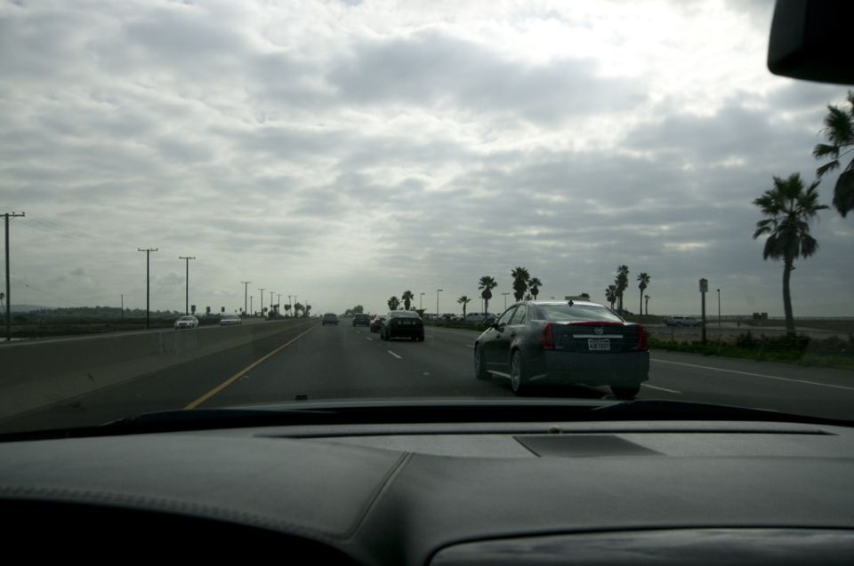 Car driving on highway with palm trees and cloudy sky. Other cars on the road