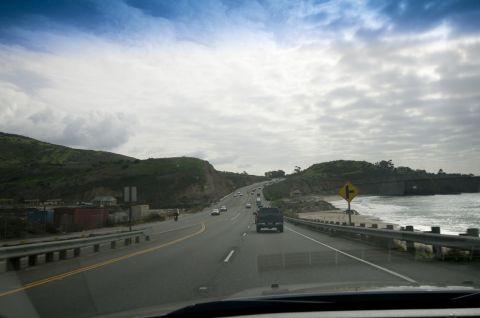 2006 Cadillac STS - A highway runs along the coast with several cars and a dark SUV ahead.