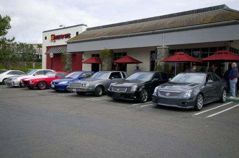 2006 Cadillac STS - A group of Cadillacs and other vehicles are parked outside a restaurant.