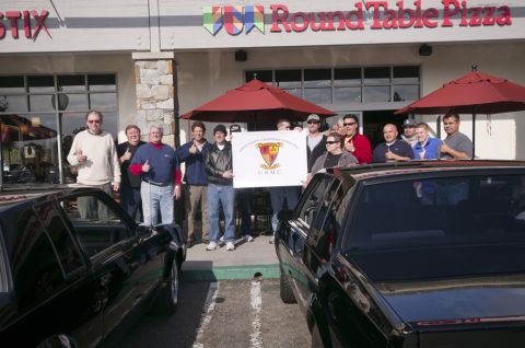 2006 Cadillac STS - A group poses with a USMC banner outside a Round Table Pizza, with two black cars visible in the foreground.