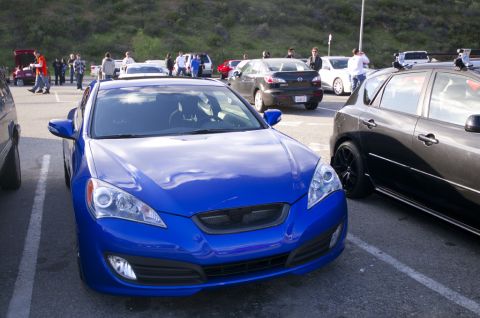 2006 Cadillac STS - A blue coupe is parked in a lot with other vehicles and people milling about.