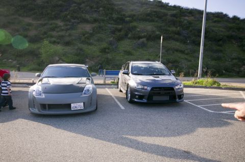 2006 Cadillac STS - A gray Nissan 350Z and a dark gray Mitsubishi Lancer Evolution are parked in a lot with a grassy hill in the background.