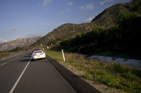 2006 Cadillac STS - Two cars driving on a highway next to a mountain range.
