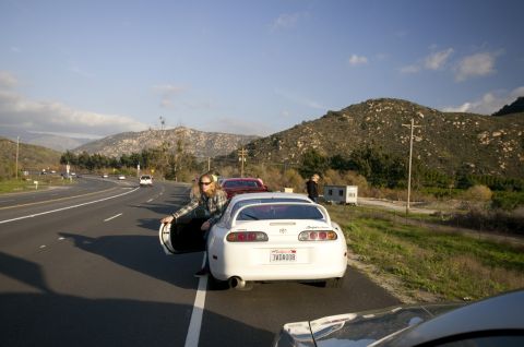 2006 Cadillac STS - A white Toyota Supra is parked on the side of a highway with mountains in the background.