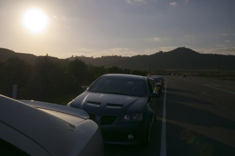2006 Cadillac STS - Several cars are parked on the shoulder of a highway as the sun sets behind rolling hills.