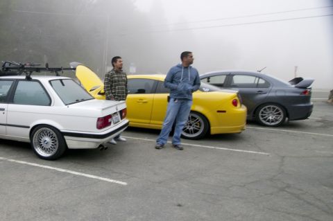 2006 Cadillac STS - Three cars are parked in a lot on a foggy day. Two men stand near the vehicles.