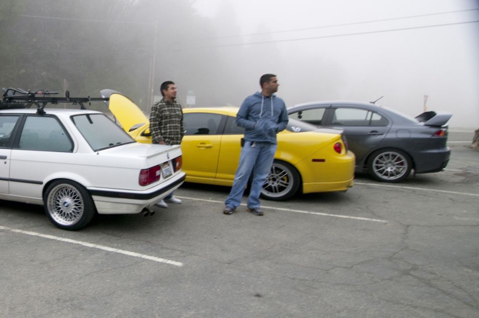 White BMW, yellow car, and gray sedan parked in a lot with two guys standing around
