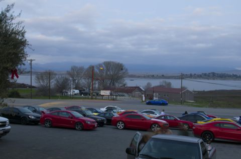 2006 Cadillac STS - A variety of cars are parked in a lot near a body of water, with buildings and hills visible beyond.