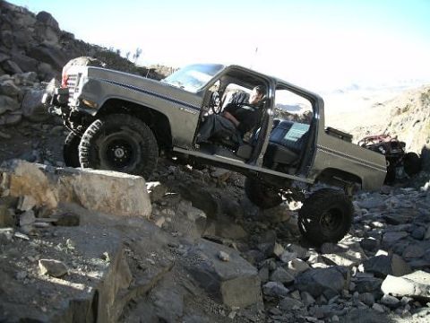 1990 Chevrolet Suburban - A lifted pickup truck navigates a rocky, off-road course with another vehicle visible in the background.