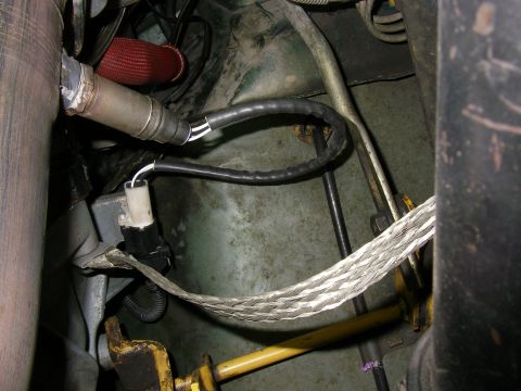 1990 Ford Bronco - Close-up of an oxygen sensor threaded into an exhaust pipe, with its black wiring lead running to a white and black electrical connector ne…