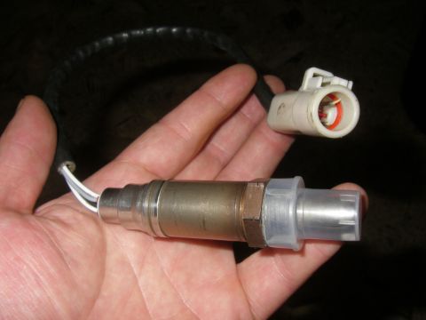 1990 Ford Bronco - A hand holds a new heated oxygen sensor with its protective clear plastic tip cover still in place, showing the hex body, stainless shell a…