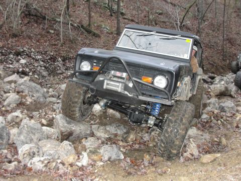 1967 Ford Mustang - Modified Ford Bronco tackling a challenging off-road course with large rocks and steep inclines.