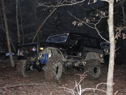 1967 Ford Mustang - A modified black SUV with off-road tires and a roll cage is seen in a forest at night.