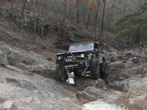 1967 Ford Mustang - This modified off-road vehicle navigates a challenging rocky path in a wooded area.