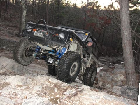 1967 Ford Mustang - A heavily modified off-road vehicle navigates a challenging rocky trail in a wooded environment.