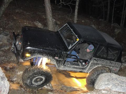 1967 Ford Mustang - A black 1977 Ford Bronco navigates a rocky trail, with its tires deep in water and mud.