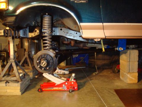 1995 Ford Bronco - Front suspension and frame of a 1995 Ford Bronco undergoing repair work in a garage.